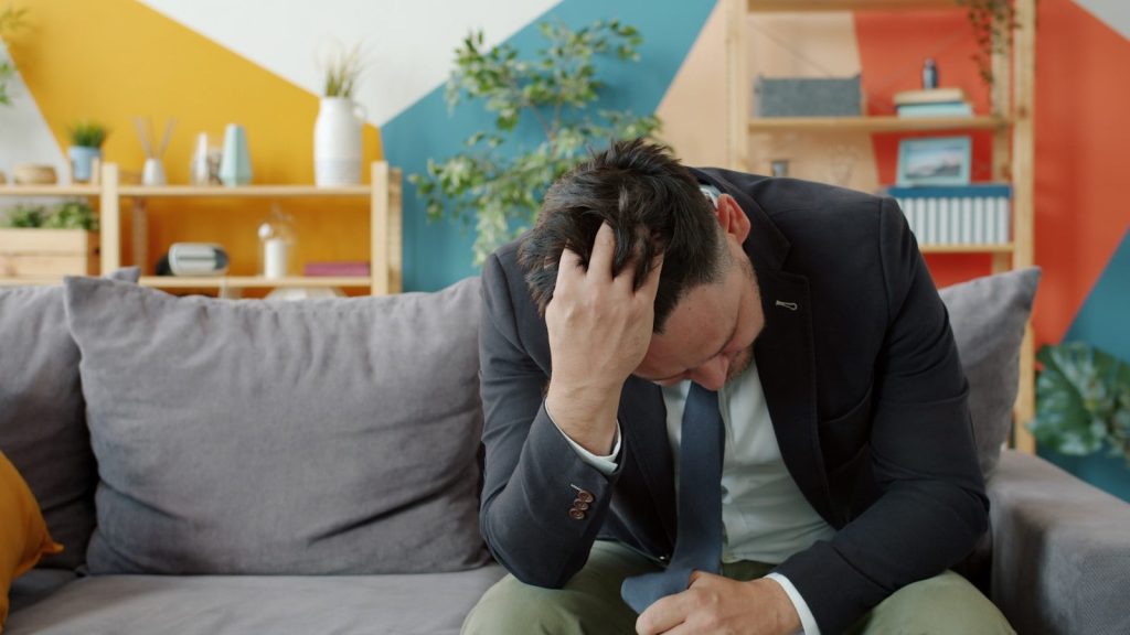 Man in suit sitting on couch with head in hands.