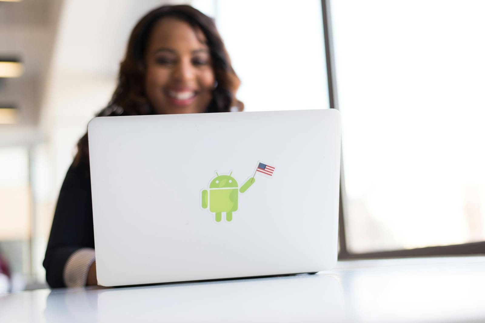 An African American woman working remotely on a laptop featuring an Android sticker in a bright office.