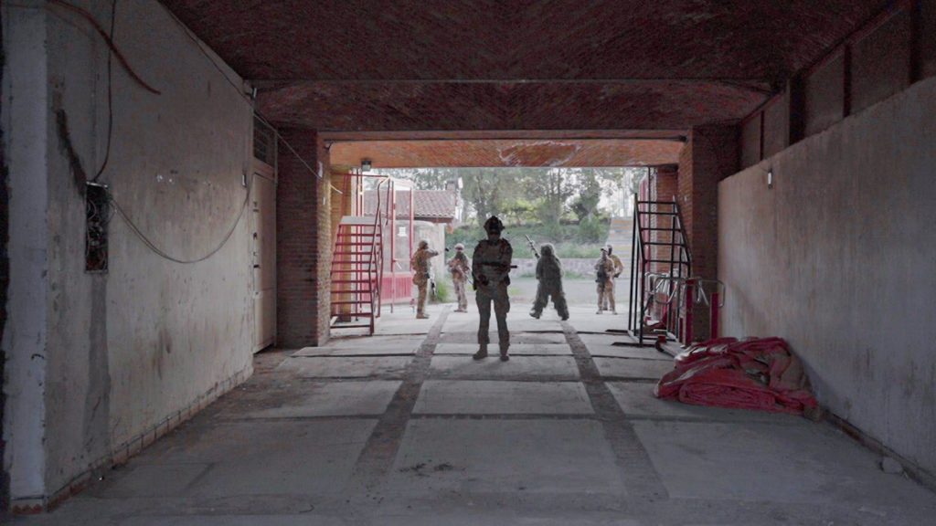Soldiers wearing camouflage uniforms in a garage setting, ready for action.