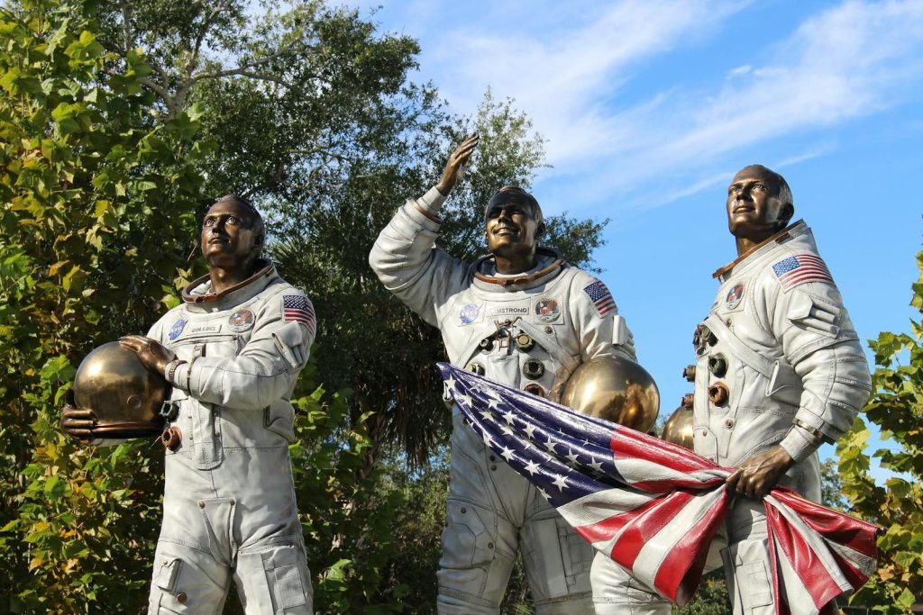 Bronze statue of Apollo astronauts at Cape Canaveral, holding a flag.