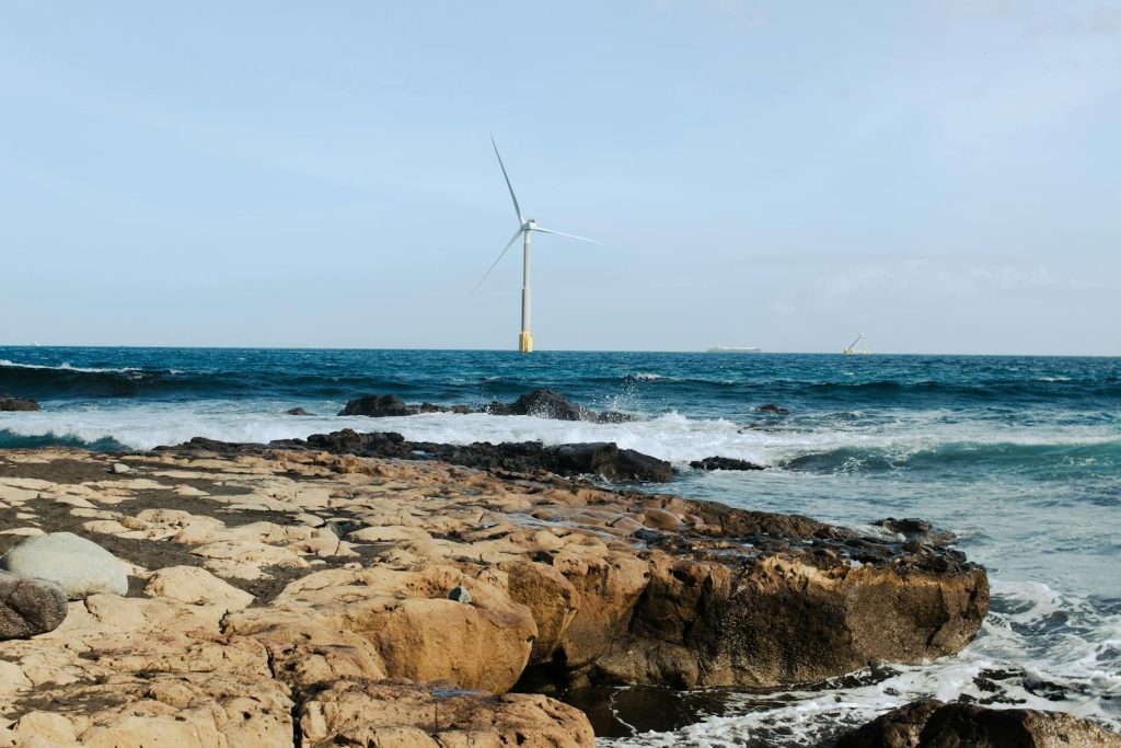 Wind turbine overlooking a rocky coastline with waves, showcasing renewable energy by the sea.