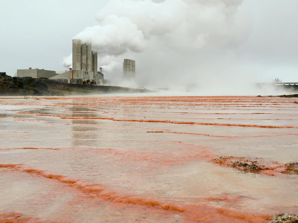 Factory with smoking chimneys by a steaming shore in Keflavík, Iceland.