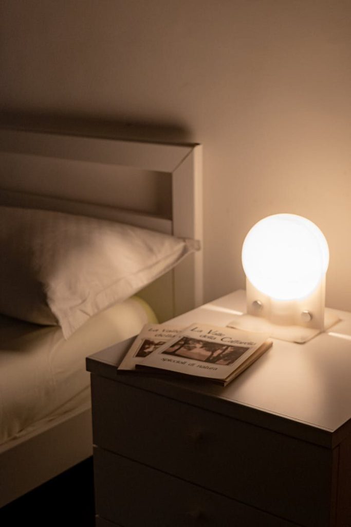 A bedside table with lamp and books creating a cozy ambiance in a minimalistic bedroom.