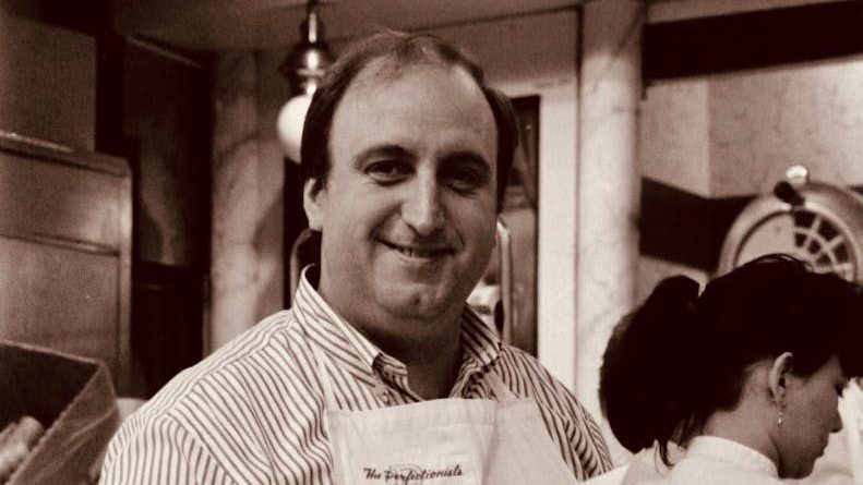 Man in apron smiling while preparing French fries at an indoor food stall.