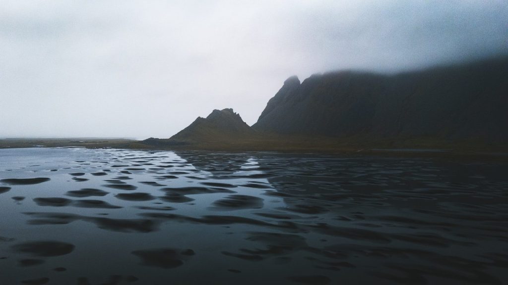 Mountains reflect in a dark, wet landscape.
