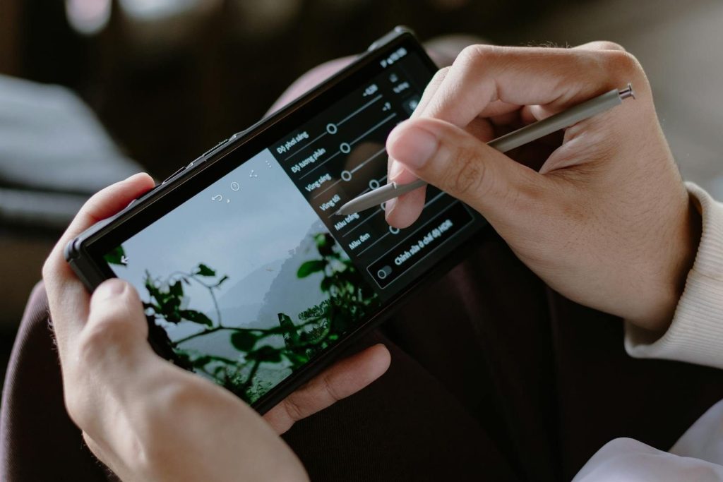 Close-up of a person editing photos on a smartphone with a stylus indoors.