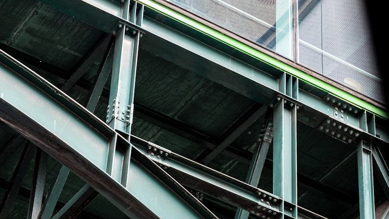 Green steel beams form an industrial bridge structure.
