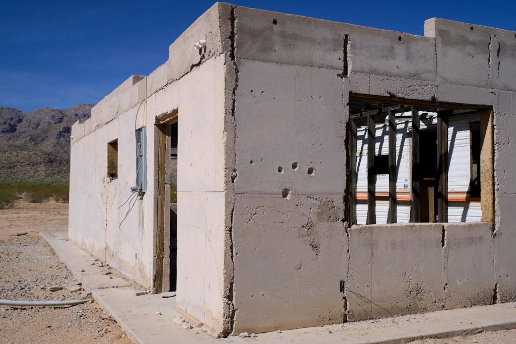 A weathered and abandoned concrete building in a vast desert under a clear blue sky.