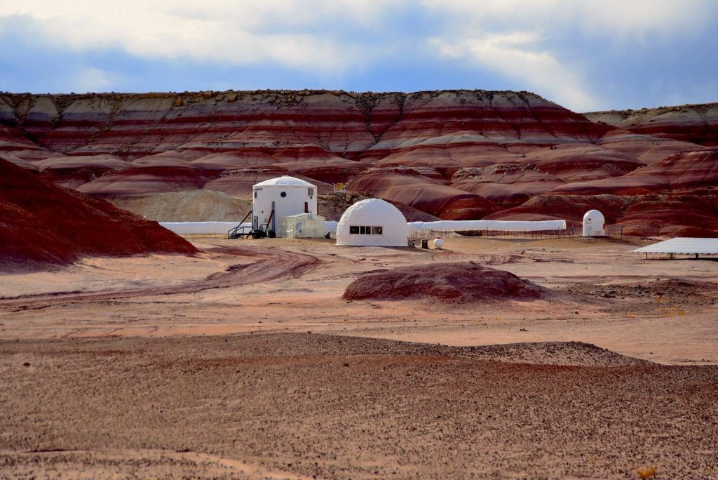 A research station in a desert landscape, resembling the surface of Mars, with red rock formations.
