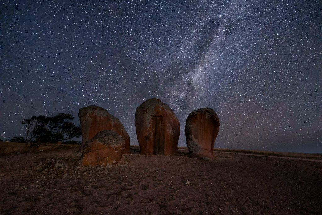 a group of rocks sitting on top of a dirt field under a night sky