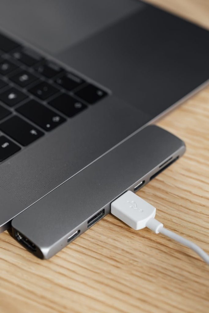 From above closeup of modern stylish thin netbook with smart usb hub equipment and connected white cable placed on wooden surface