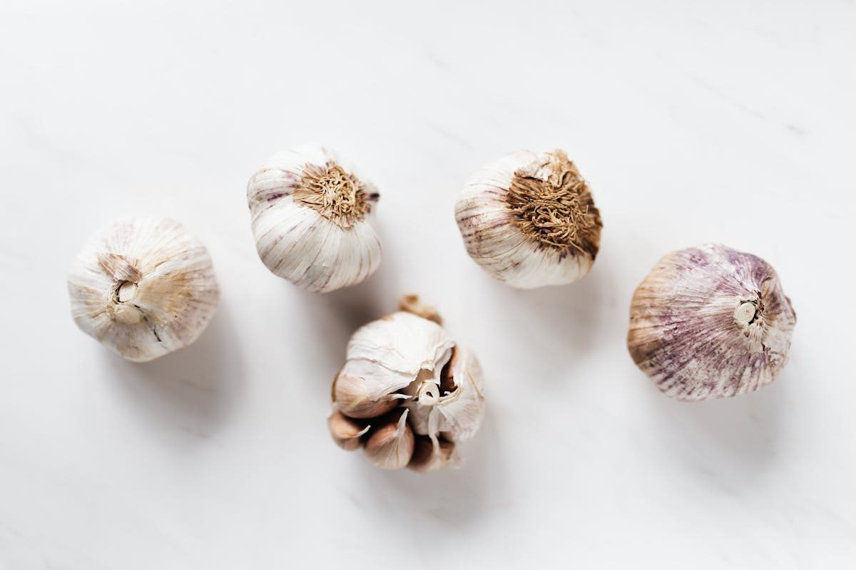 Top view of whole organic unpeeled aromatic garlic bulbs lying in row on white clean marble surface before cooking process