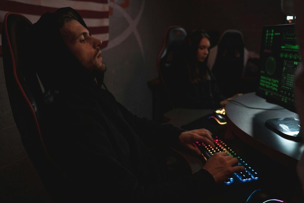 Young adults working on cybersecurity tasks in a dimly lit tech environment.
