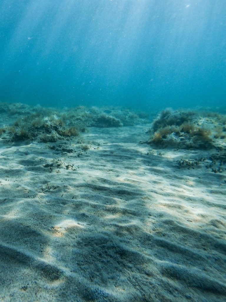 Tranquil underwater scene showcasing ocean sand and sunlight filtering through clear blue water.