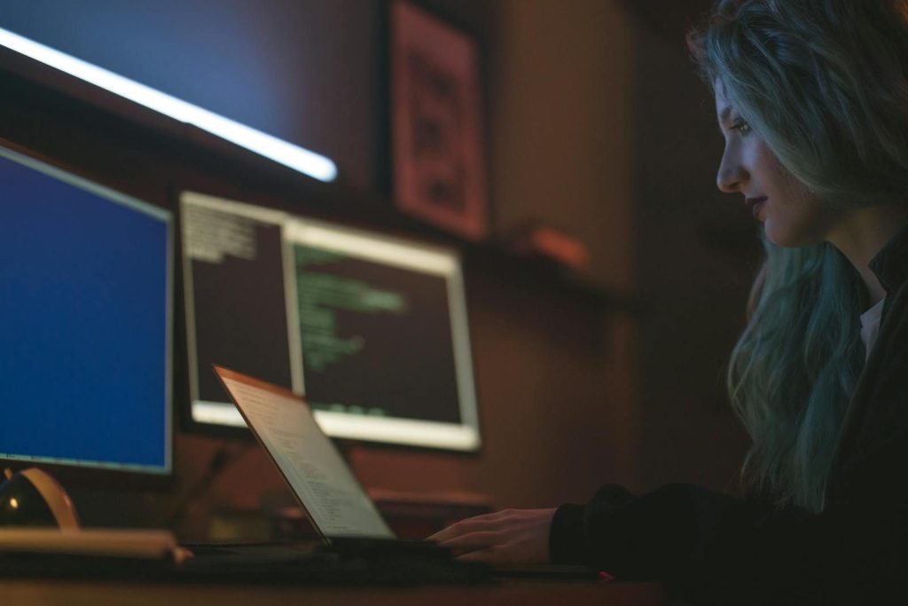 Woman working on cybersecurity programming with laptops and multiple screens