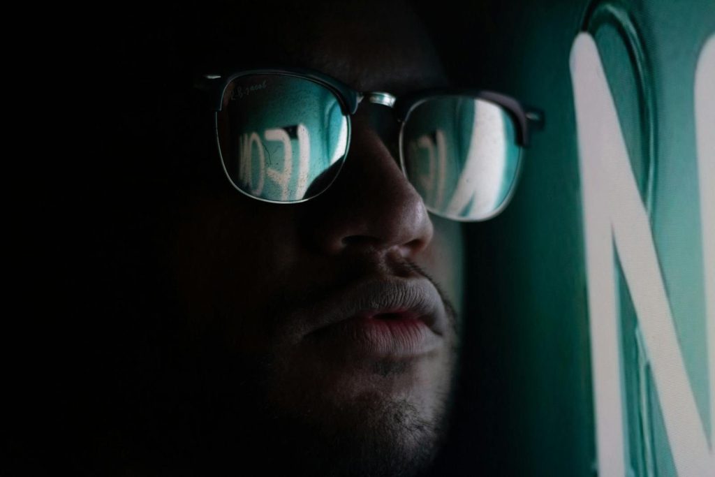 Close-up of a man wearing sunglasses reflecting neon lights, creating a mysterious mood.