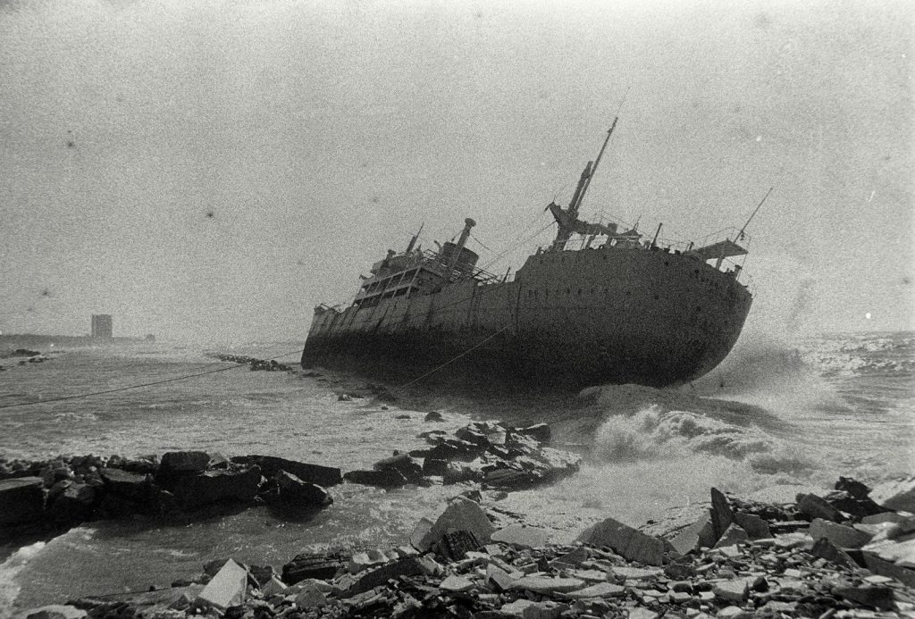 A large ship is beached by crashing waves.