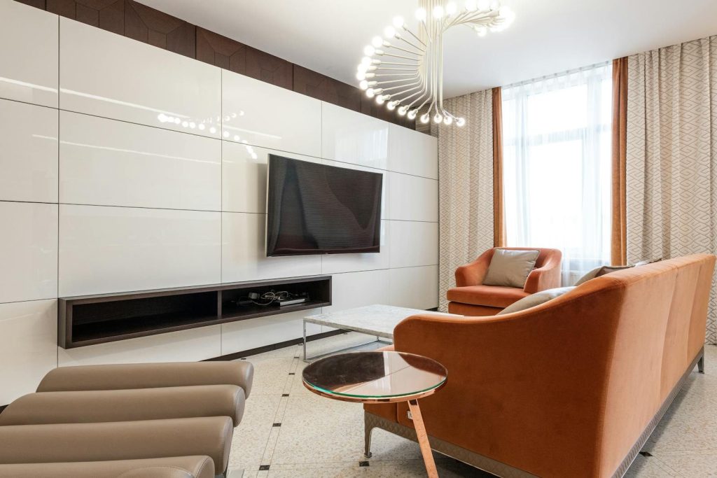 Stylish room with comfortable couch and armchair near side table placed against modern TV set in contemporary apartment with curtains on window