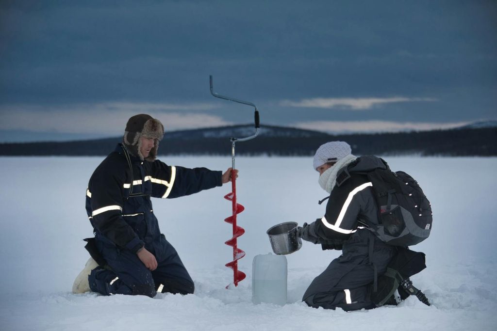 Two explorers use an ice auger on a frozen lake in Kiruna, Sweden during winter.