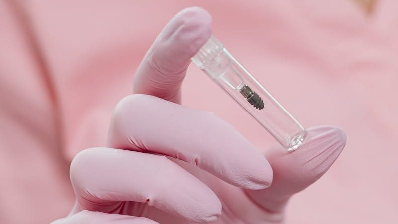 Close-up of a healthcare worker in pink uniform holding a medicine vial with gloved hands.