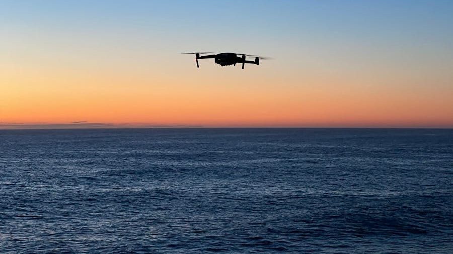 A silhouette of a drone flying over the ocean during a vibrant sunset in Tamarama, NSW.