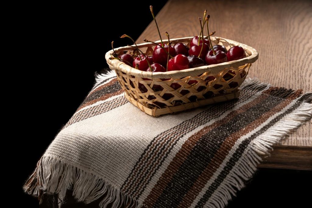 A basket filled with fresh cherries on a rustic table with a woven cloth, perfect for vibrant summer themes.