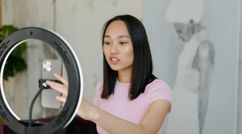 Young woman using a smartphone and ring light for social media content indoors.