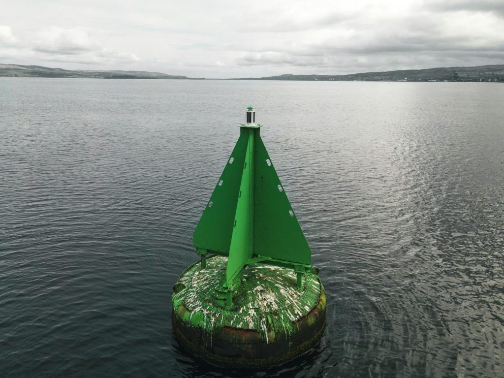 A green buoy in the calm sea near Greenock, Scotland, highlighting water navigation.
