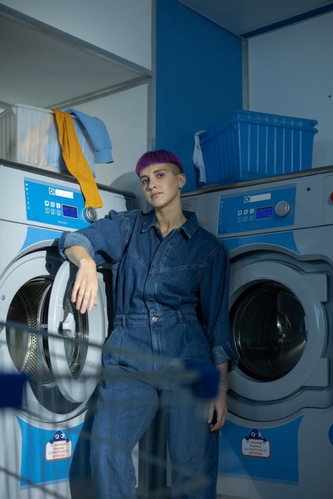 Woman in denim jumpsuit standing near washing machines at a laundromat with modern style.