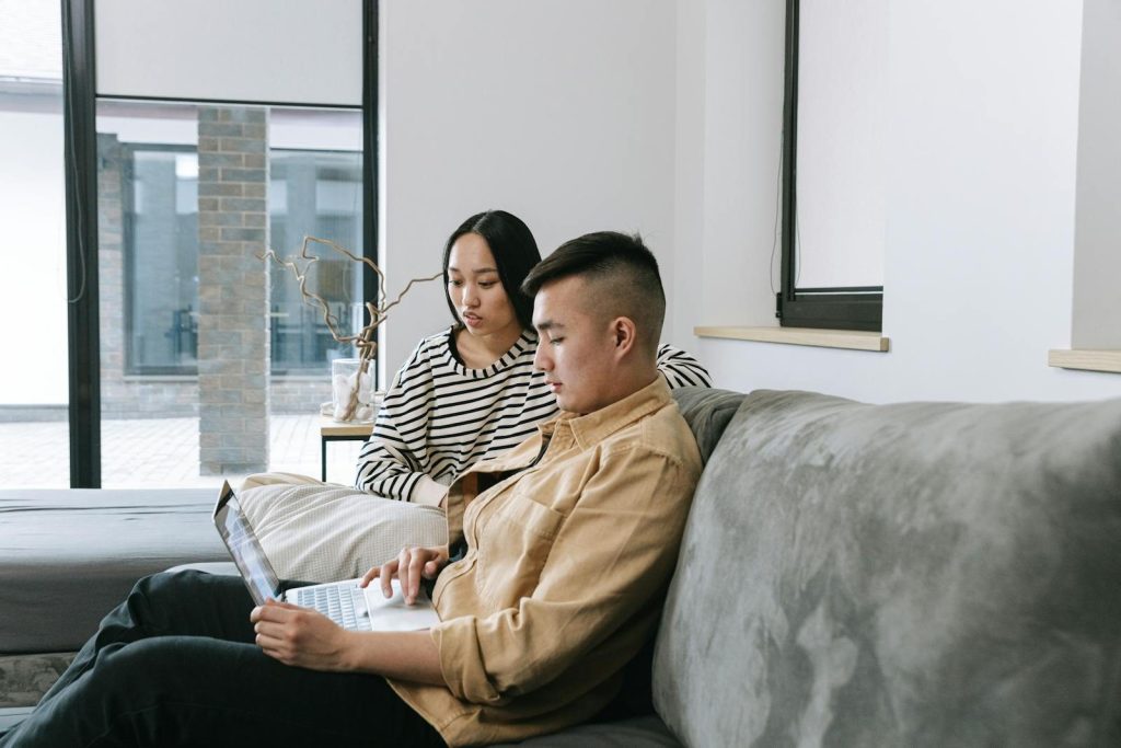 Two adults working from home in a cozy living room setting using a laptop.