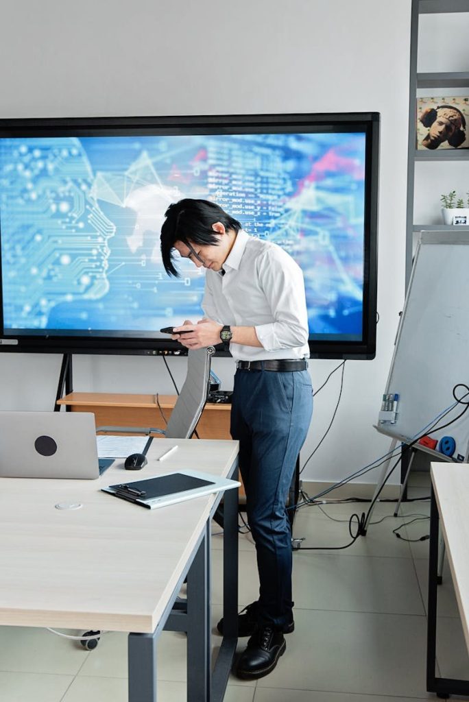 A man standing in an office checks his smartphone with a digital screen displaying AI graphics. AI