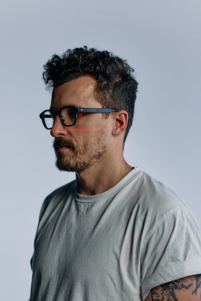 Profile portrait of a man with curly hair and glasses, against a plain studio background.