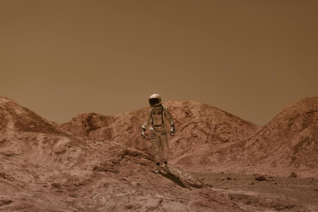 An astronaut in a spacesuit ventures across a barren, Mars-like desert landscape.