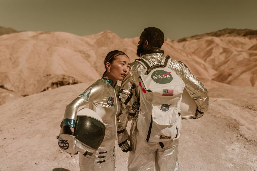 Two astronauts in silver space suits stand in a desert, depicting a Mars-like exploration scene.