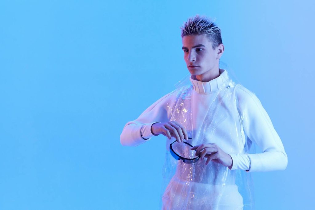 Modern male model posing in futuristic attire under blue lighting in a studio setting.