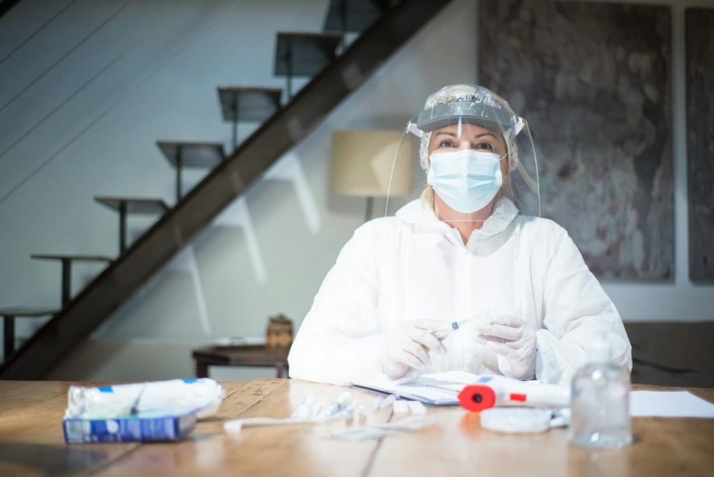 A healthcare professional in PPE and face mask holds medical equipment at a table indoors.