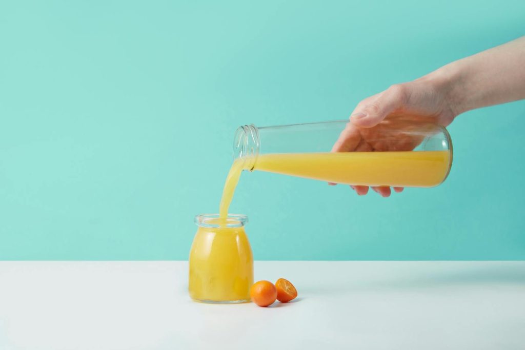 Refreshing orange juice being poured from a glass pitcher into a jar, set against a turquoise background.