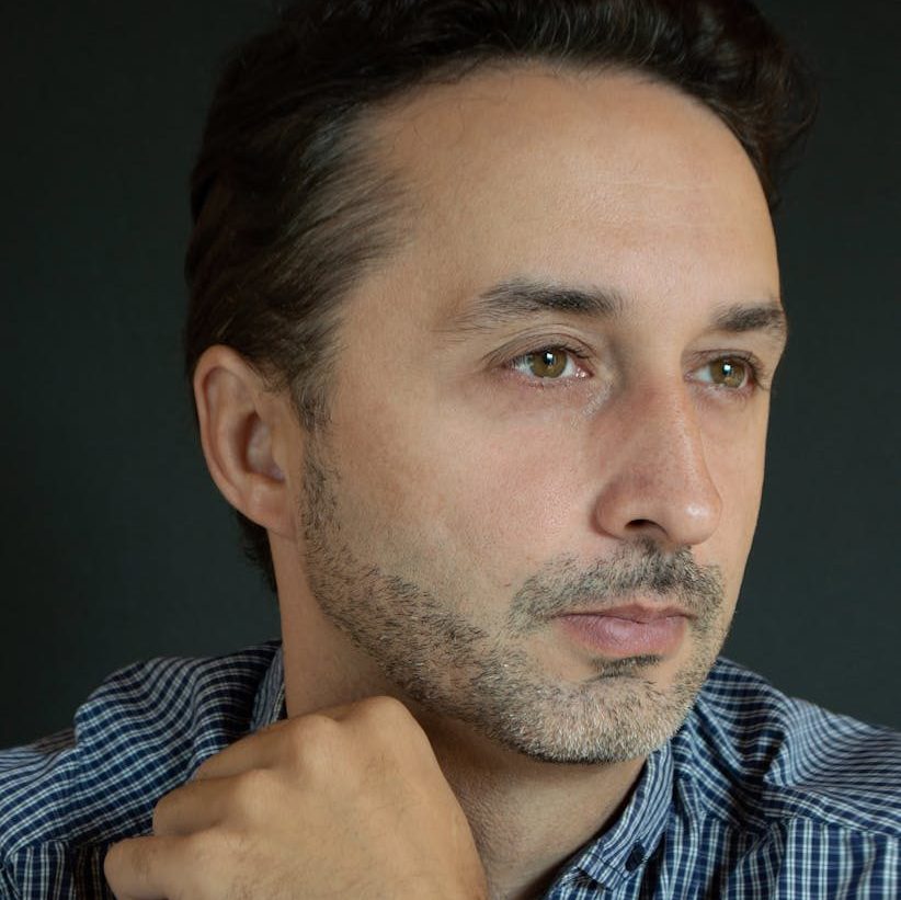 Portrait of a middle-aged man with facial hair, dressed in a checkered shirt, gazing thoughtfully.