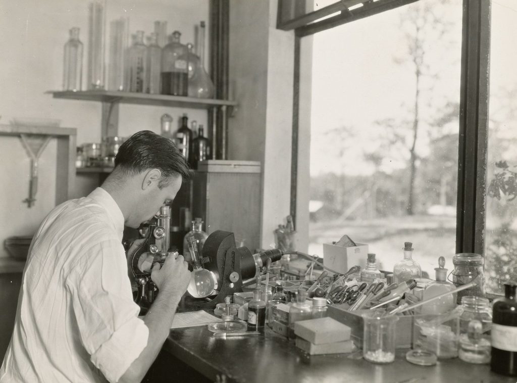 grayscale photography of scientist using microscope in the zoological division