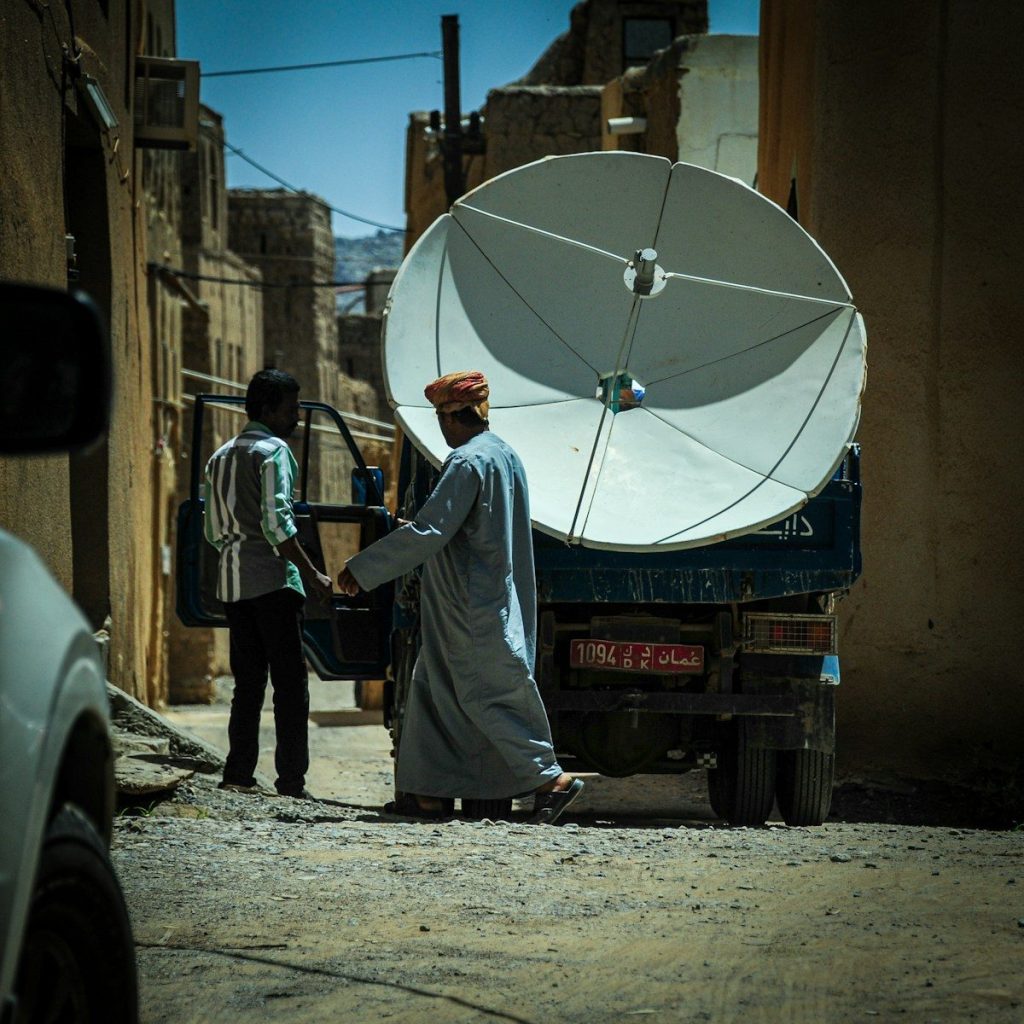 Men unload satellite dish from truck on street.