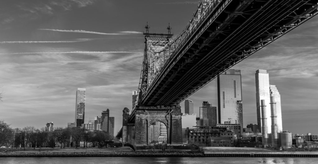 Underneath a large bridge with city skyline beyond