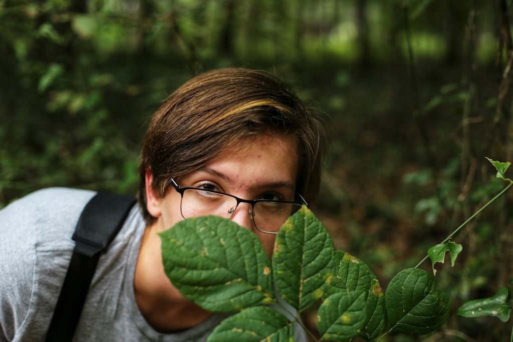 woman in gray hoodie wearing eyeglasses covering her face with green leaves