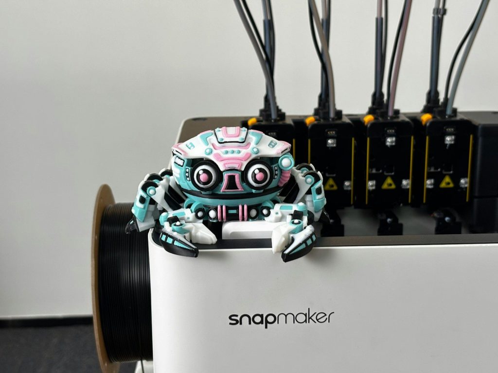 A small, colorful robot sits on a white machine.