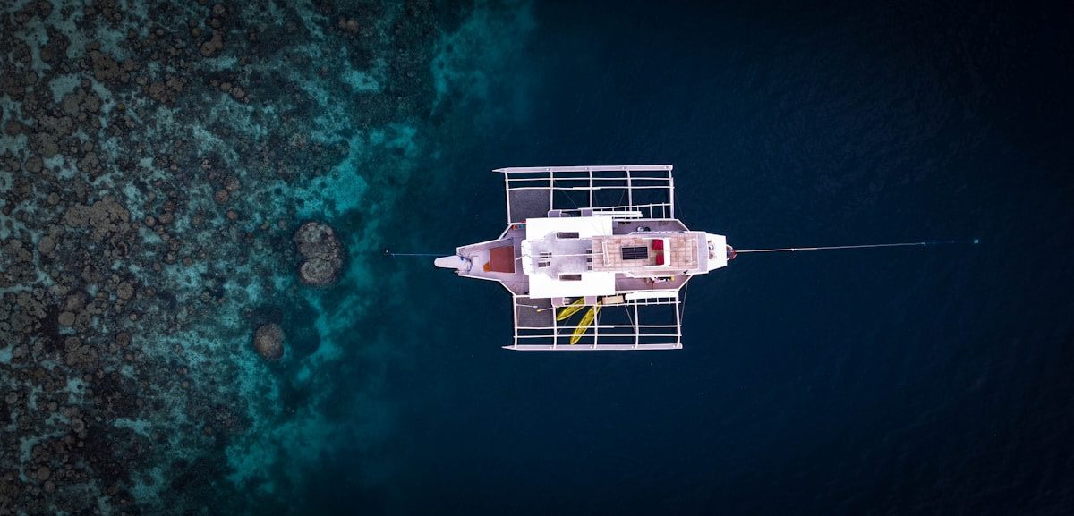White boat floats over clear blue water and coral reef.