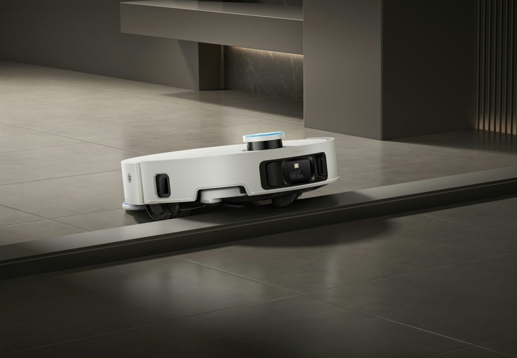 A white robot vacuum cleaner navigates a floor transition.