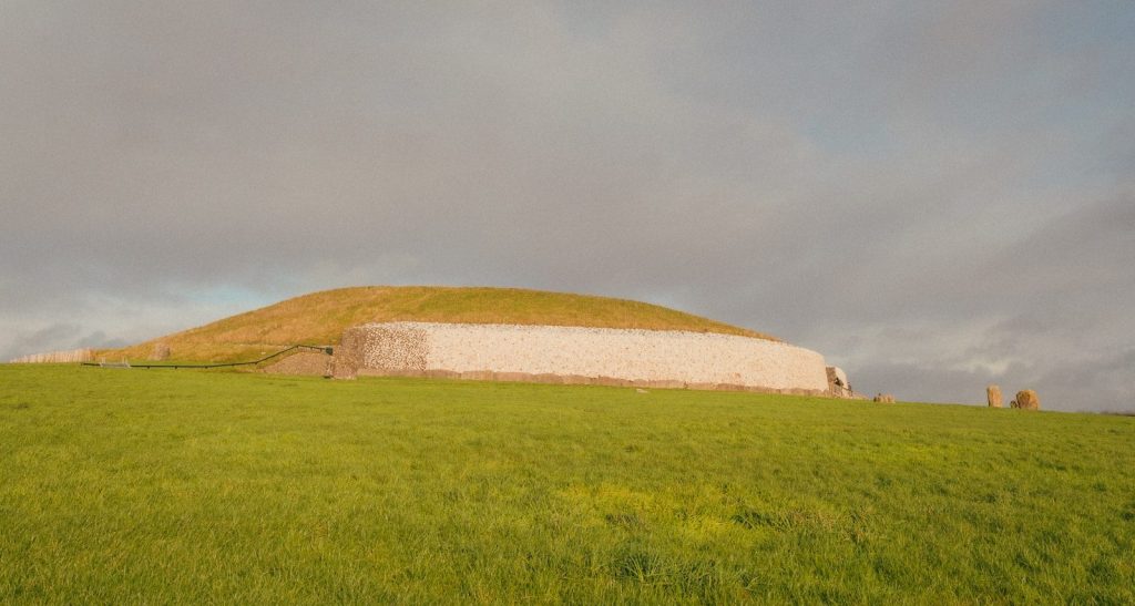 Ancient burial mound on a grassy hill under cloudy sky