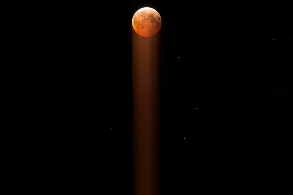 Blood moon in starry night sky with light beam