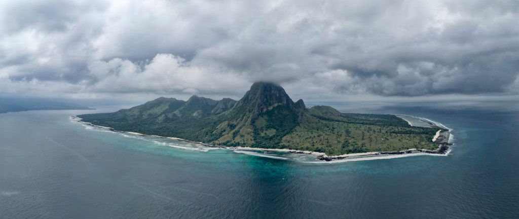 Lush green island with a prominent peak under cloudy sky.