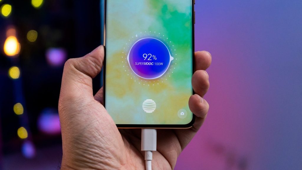 a person holding a cell phone with a charger in their hand