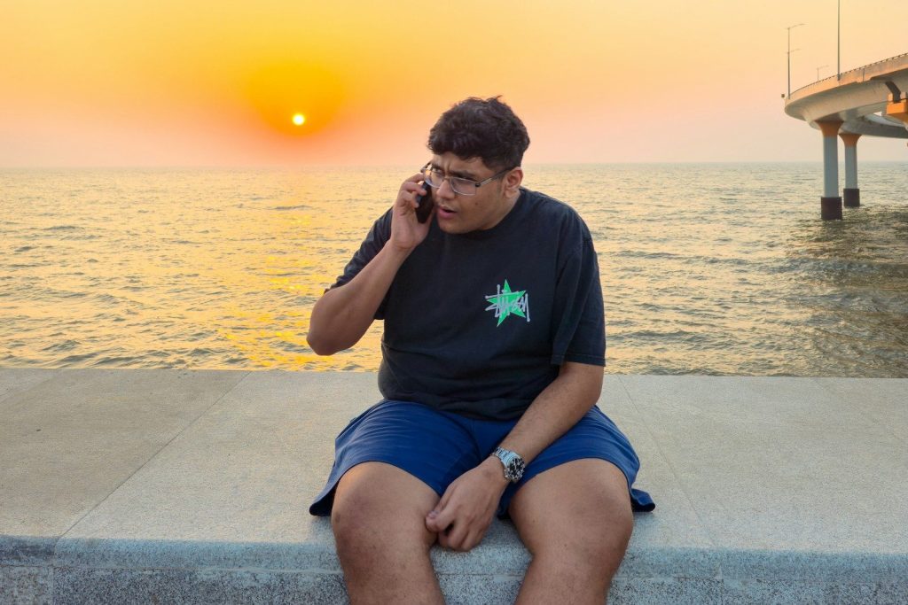 Young man talking on phone by the ocean at sunset